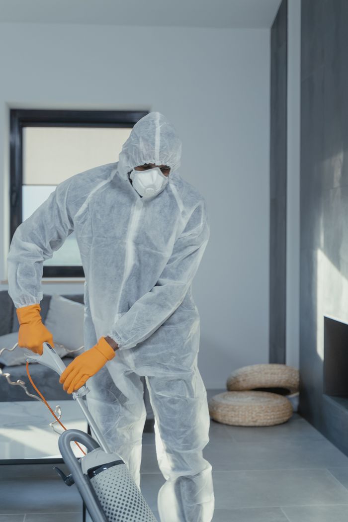 hero-02 A person in personal protective equipment vacuuming indoors, ensuring a thorough clean.