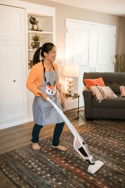 services-03 A cleaner in protective coveralls and gloves vacuuming a modern living room.